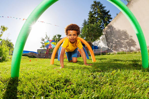 Portrait of a cute curly boy pass under obstacle course barriers playing competition game - Foto, afbeelding