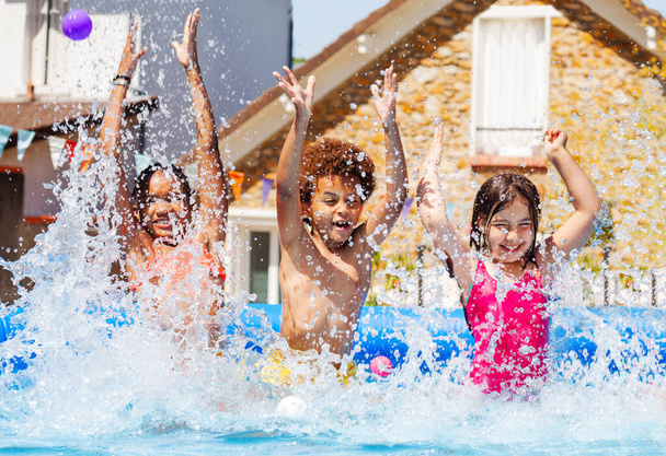 Happy group of friends little diverse kids having fun in an inflatable swimming pool in the garden splash with water - Foto, imagen