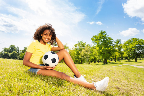 Young happy cute curly black beautiful girl with football ball sit on the grass - Fotó, kép
