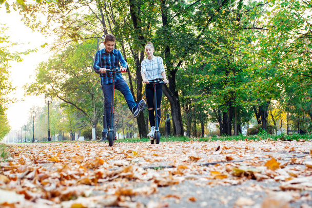 Cute teenager girl and boy riding electric kick scooter in the park. - Foto, Imagen