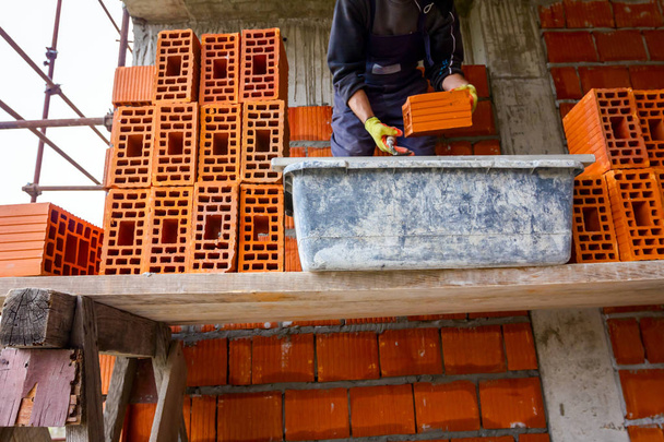 Trabajador está construyendo muro con bloques rojos y mortero
 - Foto, Imagen
