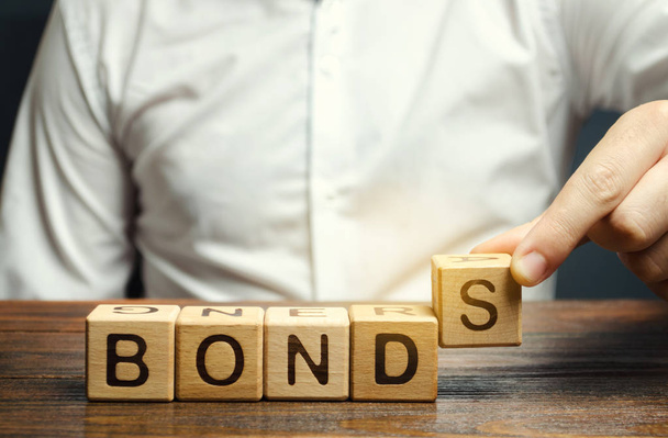 Businessman puts wooden blocks with the word Bonds. A bond is a security that indicates that the investor has provided a loan to the issuer. Equivalent loan. Unsecured and secured bonds. - Fotó, kép