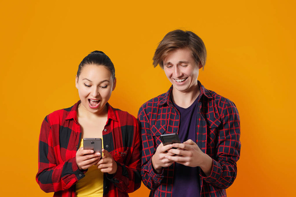 Happy young guy and girl with smartphones in hand, chatting with each other and laughing. colored yellow orange background - Fotografie, Obrázek