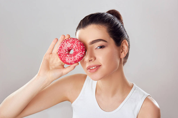 Young Girl Covered Her Face with Pink Donut in Home Kitchen. Brunette Girl Tastes a Donut. Sweets Are Unhealthy Junk Food. Dieting, Healthy Eating, Lifestyle. Weight Loss.  - 写真・画像