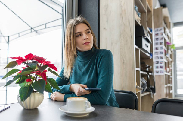 Winter portrait of woman sitting at cafe with cup of coffee - Foto, afbeelding