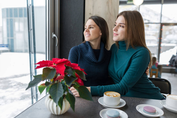 Two laughing embracing young women sitting at table in coffee shop - Fotoğraf, Görsel