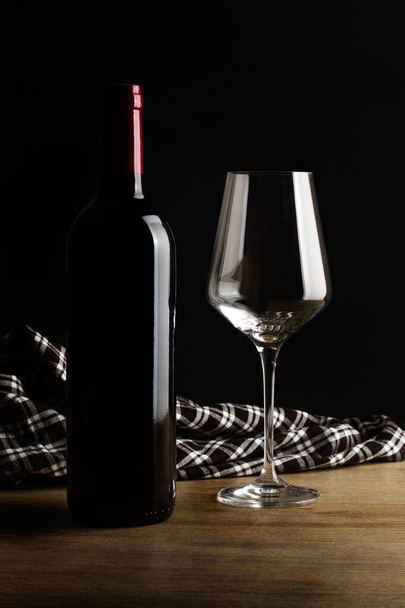 A bottle of red wine and a glass on a wooden table in a dark background - Photo, Image