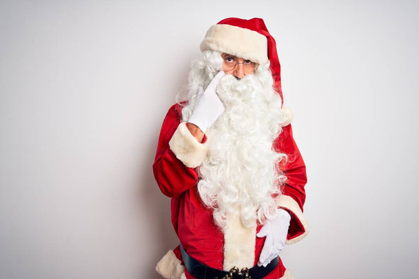 gutaussehender Mann mittleren Alters im Weihnachtsmannkostüm, der vor isoliertem weißen Hintergrund steht und auf das Auge zeigt, das dich beobachtet, Geste, misstrauischer Ausdruck - Foto, Bild
