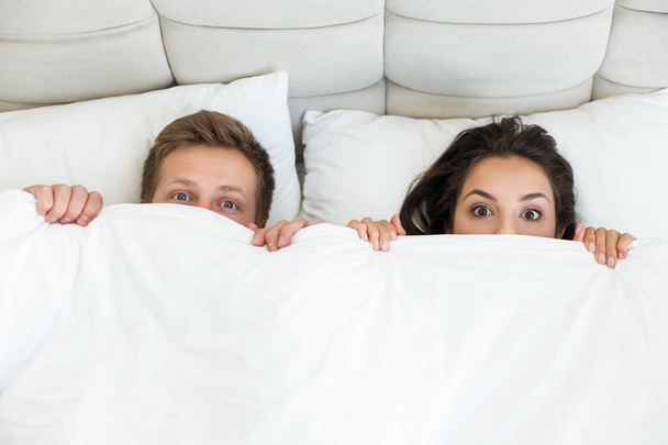 молодая пара красивый муж и его красивая жена обнимаются в постели в яркой спальне с одеялом покрывая половину их лиц семейная идиллия утром
 - Фото, изображение