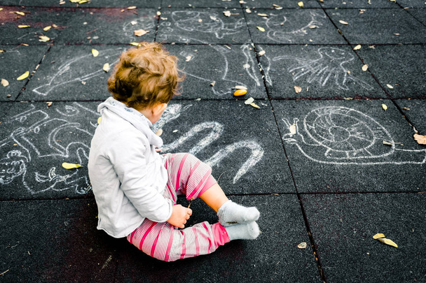 Vauva tyttö katsoo liitu piirustukset lattialla playgr
 - Valokuva, kuva