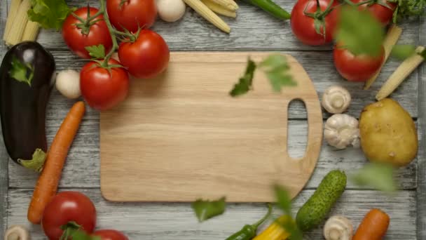Trozos de perejil cayendo sobre una tabla de cortar con verduras alrededor - Imágenes, Vídeo