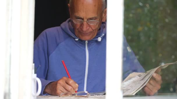 senior man solves crossword on window sill slow motion - Séquence, vidéo