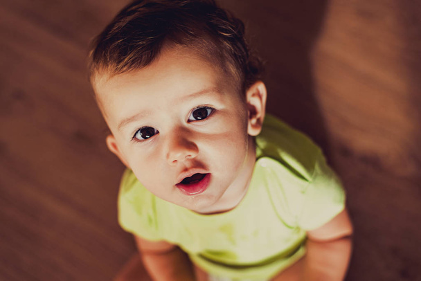 Μωρό κάθεται κοιτάζοντας προς την κάμερα πάνω του με περιέργεια - Φωτογραφία, εικόνα