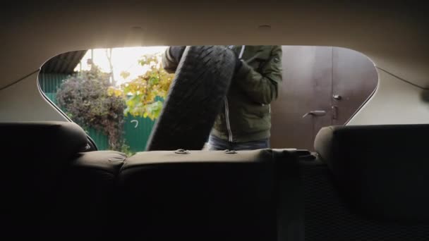 Egy férfi téli gumikat tesz egy kocsi csomagtartójába. - Felvétel, videó