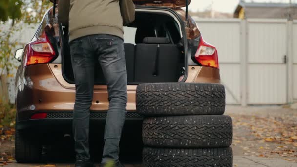 Egy férfi téli gumikat tesz egy kocsi csomagtartójába. - Felvétel, videó