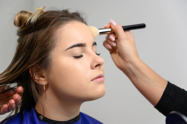 Studio photo of the work of a makeup artist by a hairdresser beautician. Creating beautiful makeup and hairstyles, rejuvenating the skin of the face. The professional is working with special tools. - Фото, изображение