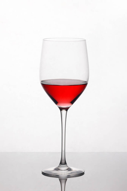 red wine swirling in a wine glass standing against light background - Фото, изображение