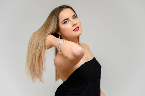 Studio portrait of a beautiful girl with long beautiful hair and excellent make-up on a gray background in different poses. She smiles. - Foto, imagen