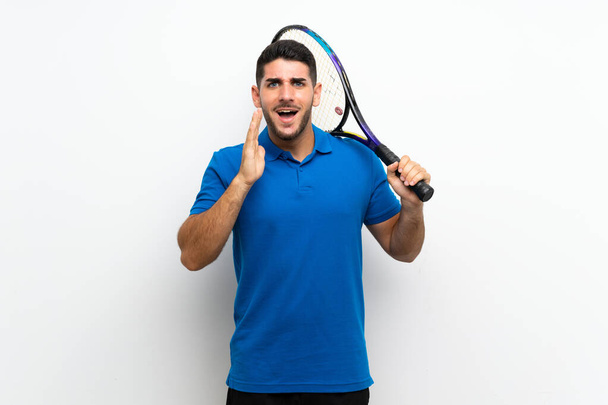 schöner junger Tennisspieler Mann über isolierte weiße Wand mit Überraschung und schockiertem Gesichtsausdruck - Foto, Bild
