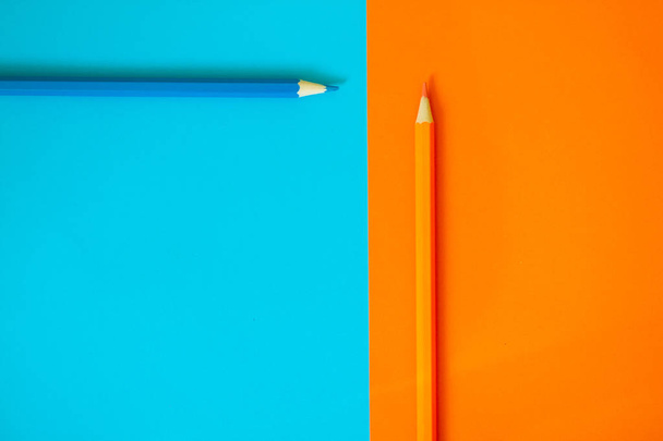 Two pencils - orange and cyan on colored paper in blue and yellow.  - Фото, зображення