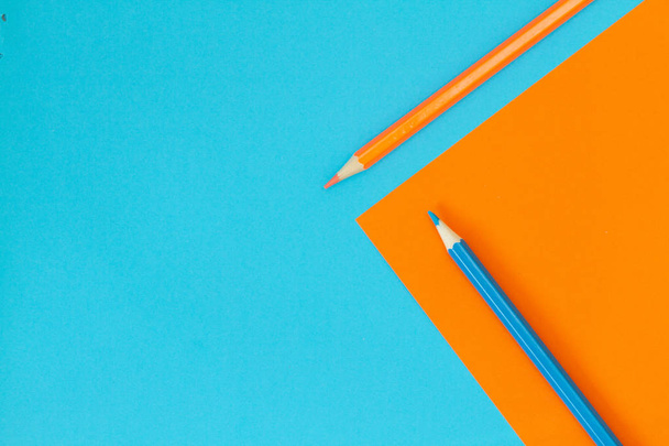 Δύο μολύβια - πορτοκαλί και κυανό σε χρωματιστό χαρτί σε μπλε και κίτρινο.  - Φωτογραφία, εικόνα
