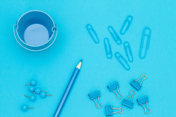 Papelería sobre fondo azul. Cubo azul, clips, lápiz y botones - disparado desde arriba
 - Foto, Imagen
