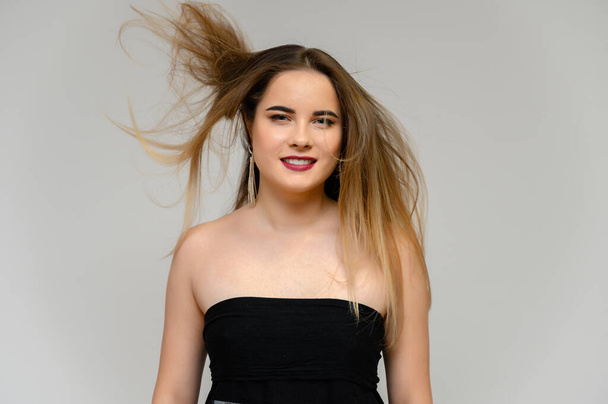 Studio large photo portrait of a beautiful girl with long beautiful flowing hair and excellent make-up on a gray background in different poses. She smiles. - Foto, Bild