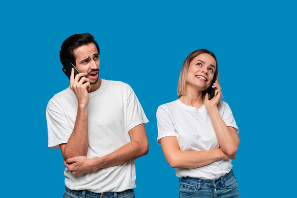 Blond woman and brunet man in white tees and blue jeans are talking on the phone. - 写真・画像