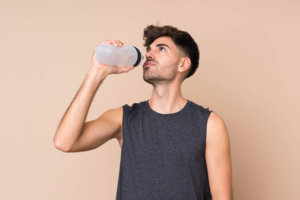 Νεαρός άνθρωπος του αθλητισμού πάνω από απομονωμένο φόντο με σπορ μπουκάλι νερό - Φωτογραφία, εικόνα