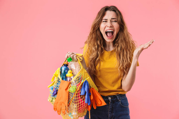 Photo of angry young woman holding bag with plastic waste and shouting - Фото, изображение