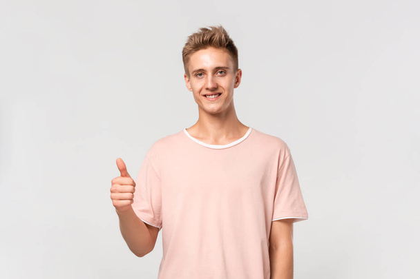 Mosolygós jóképű fiatalember rózsaszín pólóban, hüvelykujjával felfelé mutatva az értékelését.. - Fotó, kép