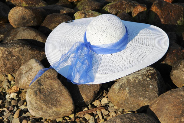 un sombrero femenino blanco con ala ancha y cinta azul en piedras ríos Banco
 - Foto, Imagen