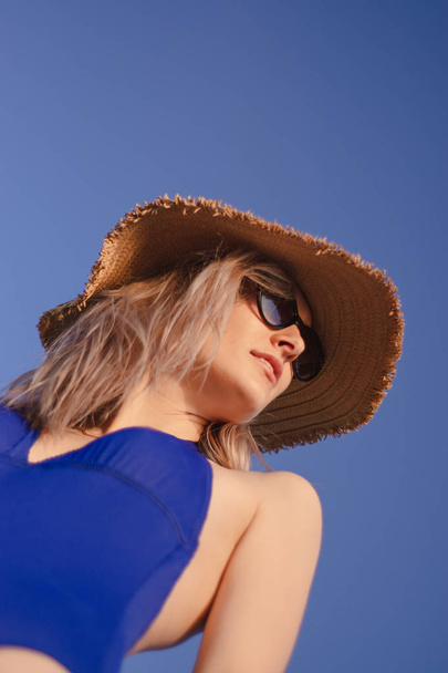Güneş doğarken plajda şapka ve güneş gözlüğü takmış genç bir kadının portresi. - Fotoğraf, Görsel