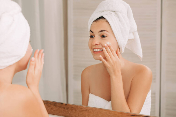 woman applying cream on her face in bathroom - Фото, зображення