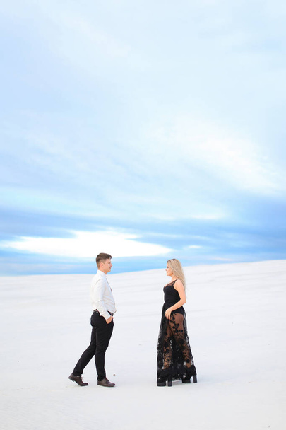 Joven hombre caucásico en camisa blanca y mujer con vestido negro caminando en la estepa de invierno
. - Foto, Imagen