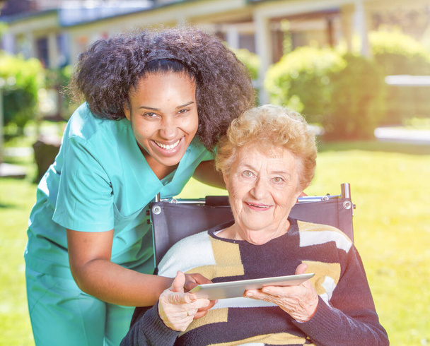 Médica ajudando idosos aposentados com tablet no jardim do hospital. - Foto, Imagem