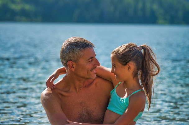 Отец и дочь на отдыхе на берегу озера смотрят друг на друга с любовью. Концепция путешествий, отдыха и отпусков - Фото, изображение