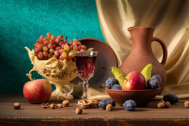 Natura morta con brocca di argilla fatta a mano, uva in vaso, prugne, mele, noci, pere e un bicchiere di vino
 - Foto, immagini