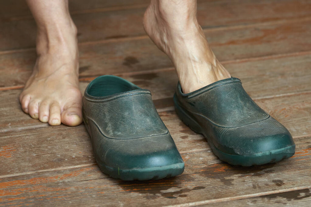 Mujer descalza pone botas de goma en pie sobre un piso de madera
 - Foto, Imagen