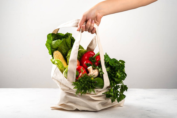 Концепция нулевых отходов. Женская рука с тканевой эко-сумкой, полной органических свежих овощей
. - Фото, изображение