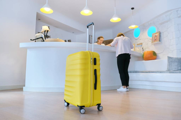 Yellow suitcase near reception desk in hotel lobby - Zdjęcie, obraz
