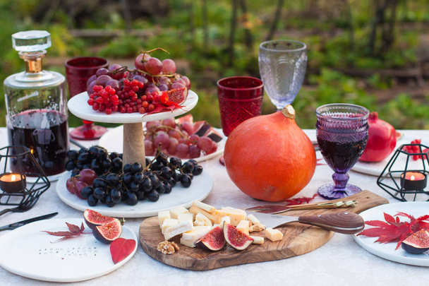 Decorated garden picnic table with bottle of wine, glasses, grapes, pumpkins, figs, charcuterie and cheese board and red berries and maple leaves.  Outside location.  - Foto, afbeelding