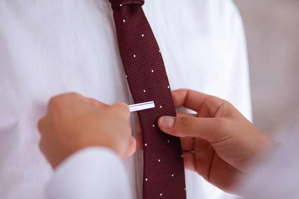 Primer plano de dos manos ayudando con la corbata a un novio en su boda
 - Foto, imagen