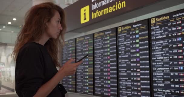 Mujer usando smartphone en el aeropuerto. Joven viajero caucásico comprobando la hora de embarque con la aplicación de teléfono móvil en la terminal
. - Metraje, vídeo