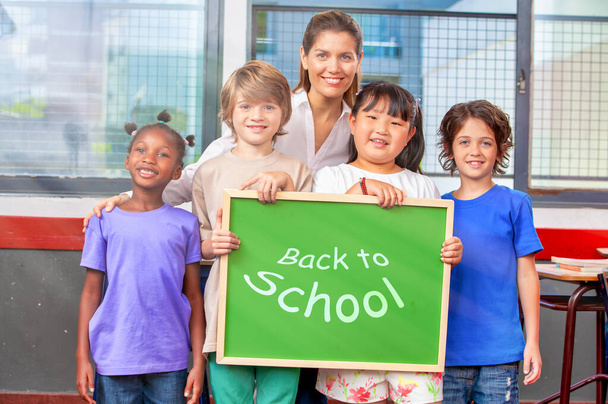 Multietnické základní spolužáky s učitelem držícím zelenou tabuli. Zpět do školy čas a koncept - Fotografie, Obrázek