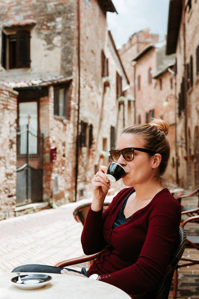 Young woman enjoying coffee in in a cafe in medieval town in Tuscany, Italy  - Foto, imagen