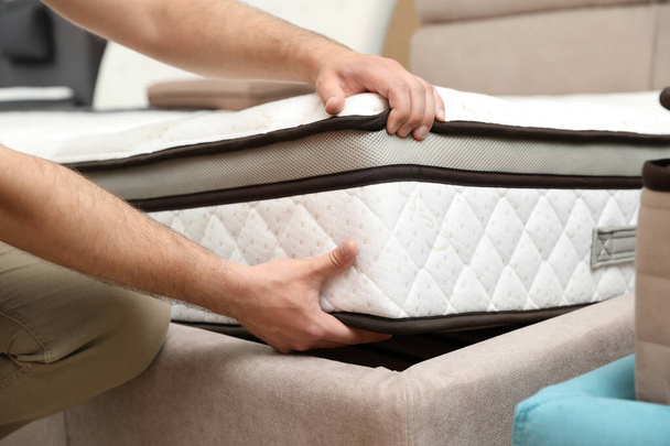 Young man choosing new orthopedic mattress in store, closeup - Foto, Imagem