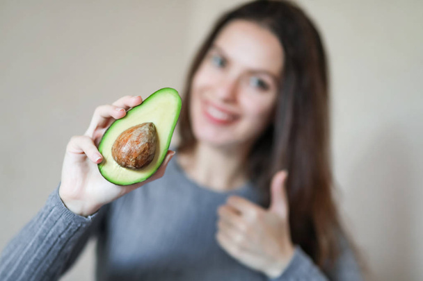 Young woman holds half of fresh ripe avocado in her hand close-up. Healthy eco food. Product of organic farming. Freshly harvested fruits. Blurred background, macro. - Foto, Imagem