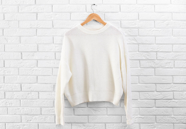 Hanger with stylish sweater on brick wall - Foto, imagen