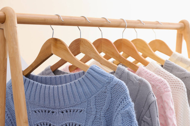 Collection of warm sweaters hanging on rack near color wall, closeup - 写真・画像